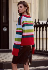 Multicolored sweater featuring broad stripes in red, green, pink, and blue. Ribbed red hem. Paired with a black leather pencil skirt.