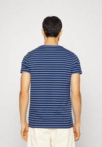 Námořnické a modré pruhované tričko s krátkým rukávem, s kulatým výstřihem a měkkým bavlněným materiálem, viděné zezadu na modelce.