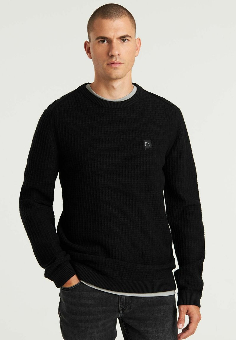 Maglione nero con un design a nido d'ape testurizzato, scollatura rotonda e maniche lunghe. Presenta una piccola toppa con logo sul lato sinistro superiore.