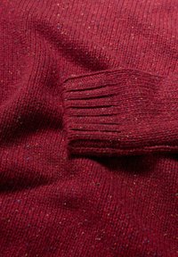 Raitapintainen burgundivärinen neulepaita, jossa on ribbireunat. Moniväriset pilkut kankaan läpi lisäävät yksityiskohtia kokonaisuuteen.