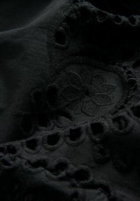Schwarzer bestickter Stoff mit floralen Mustern und Ausschnittdetails, unterschiedlichen Texturen und aufwendigen Nähten.
