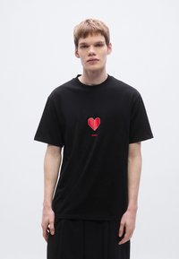 Μαύρο βαμβακερό t-shirt με σχέδιο κόκκινης καρδιάς οριγκάμι και κείμενο "HUGO" από κάτω. Κοντά μανίκια και άνετη εφαρμογή.