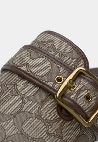 Brunt og beige vævet stof med et geometrisk mønster, med en blank guldbæltespænde og læderrem detaljer.