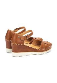 Sandales compensées en cuir marron avec des brides entrecroisées, une sangle de cheville réglable et une semelle en caoutchouc texturé blanc. Détails de couture visibles.
