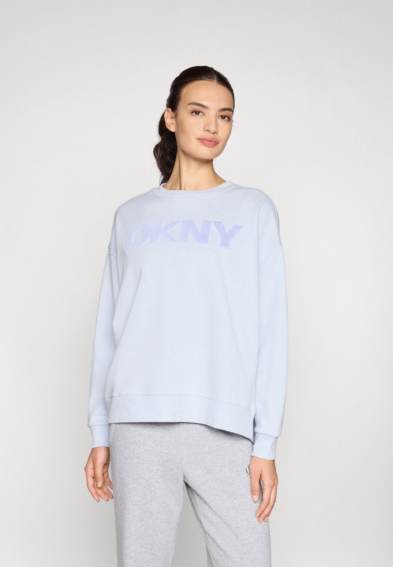 Jasnoniebieska bluza z teksturowanym logo "DKNY" w nieco ciemniejszym odcieniu. Posiada okrągły dekolt i luźne długie rękawy.
