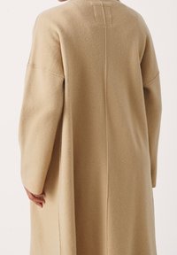 Beige wollen jas met een relaxte pasvorm, verlaagde schouders en een middennaad detail. Soepele textuur en oversized mouwen.
