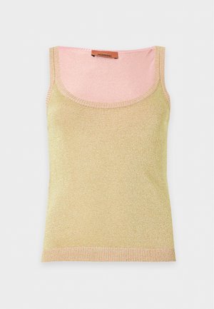 Vrouw staand, draagt een gele mouwloze top en pastelgekleurde, sprankelende wijde broek met open teenhakken.