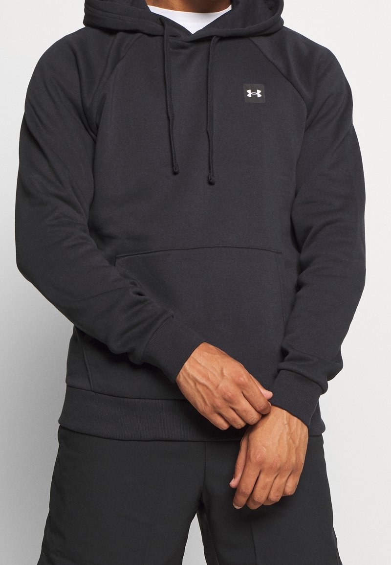 Uomo che indossa un hoodie nero di Under Armour con tasca frontale e stringhe, che aggiusta la manica con vene visibili sulle mani.