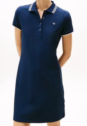 Mørkeblå polokjole med korte ærmer, hvidstripet krave og et lille emblem på brystet. Fremstillet af blødt, glat stof med minimal struktur.