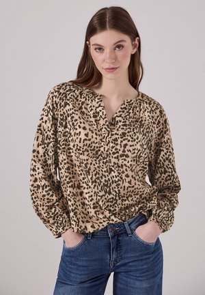 Blouse beige avec un imprimé léopard marron foncé, décolleté en V et coupe ample, portée avec un jean en denim bleu.