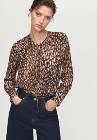 Blusa con stampa animale marrone, colletto rotondo, spalle arricciate e dettaglio con nodo frontale, abbinata a jeans in denim scuro a vita alta.