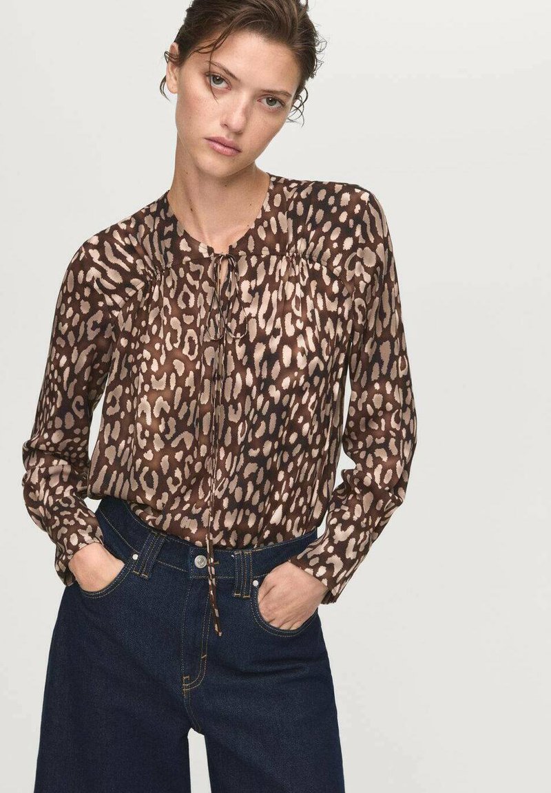 Blusa con stampa animale marrone, colletto rotondo, spalle arricciate e dettaglio con nodo frontale, abbinata a jeans in denim scuro a vita alta.