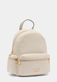 Cremfarbener Leder-Rucksack mit runder Form, goldenen Reißverschlüssen und einer Fronttasche. Mit dem Markenlogo, das an der Vorderseite in der Nähe der Unterseite geprägt ist.