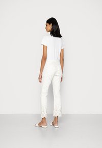 Calças brancas com padrão florido e detalhe em renda escalope na bainha, combinadas com uma t-shirt branca simples e sandálias rasas.