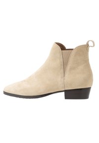 Beige suede nilkkurit, joissa on elastiset sivupaneelit, vetotappi takana, teräväkärkinen muotoilu sekä matala pinoa korko. Suora pinta, yksinkertainen muotoilu.