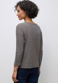 Grijs T-shirt met lange mouwen en horizontale zwarte strepen, met een ronde halslijn en een relaxte pasvorm, gecombineerd met donkerblauwe jeans.