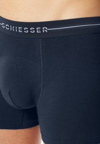 Tmavě modré boxerky s měkkým elastickým pasem s nápisem "SCHIESSER". Hladký povrch a přiléhavý střih s tvarujícími švy.