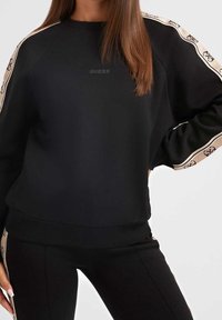 Sudadera negra con mangas raglán, con una banda texturizada a lo largo de los hombros con un patrón de logotipo, puños y dobladillo acanalados.