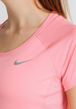 Zbliżenie osoby noszącej różową sportową koszulkę Nike z szarym logo swoosh na piersi, pokazujące dekolt i krótki rękaw.