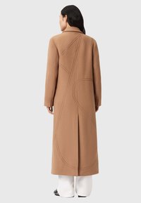 Μακρύ, καμηλό παλτό με στενή γραμμή, με σχέδιο σε seams στην πλάτη και πλαϊνές σχισμές για ευκολία κίνησης. Κατασκευασμένο από υφαντό ύφασμα.