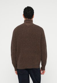 Brun tekstureret sweater med høj krave, løs pasform og lange ærmer, der har forskellige nuancer for et subtilt mønster.