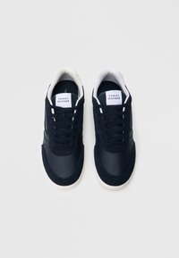 Námořnicky modré tenisky s hladkým koženým a síťovaným svrškem, bílými tkaničkami a bílou gumovou podrážkou. Na jazyku jsou umístěny štítky s logem.