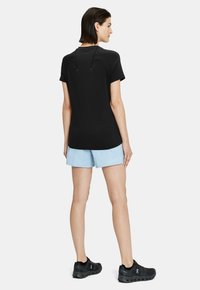 Camiseta atlética negra de manga corta y cuello redondo, combinada con pantalones cortos azul claro. El modelo lleva zapatillas de correr negras.