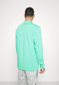 Mintgrön långärmad skjorta i bomull, med en svart Nike-logotyp på ryggen. Mjuk textur med en avslappnad passform.