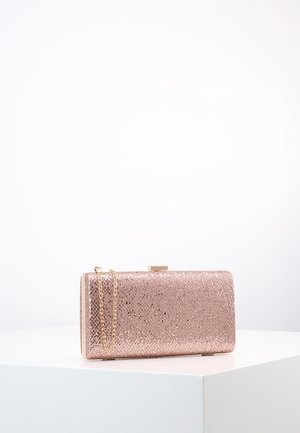 Suorakaiteen muotoinen ruusukultainen glitter-ileo, jossa kultainen ketjuhihna, lepää valkoisella pinnalla yksiväristä valkoista taustaa vasten.