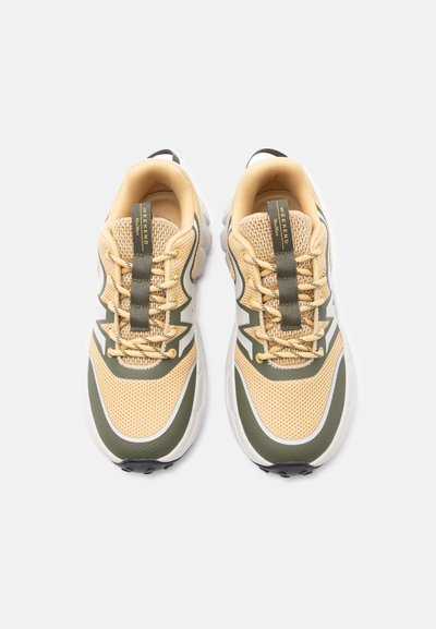 Ζευγάρι από μπεζ και ελιά πράσινα πλεκτά αθλητικά παπούτσια με κορδόνια και θηλιές επάνω γράφει "WEEKEND" σε λευκό φόντο.