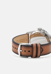 Bracelet de montre en cuir marron avec une boucle en métal argenté, présentant des coutures contrastées et une texture lisse, conçu pour le confort et l'ajustabilité.