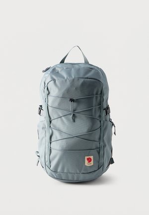 Rucsac bleu deschis cu cordon elastic frontal, curele cu cataramă pe laterale, mâner superior și patch logo roșu în centrul jos.