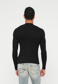 Schwarzes, figurbetontes Langarmshirt mit Rippstruktur und rundem Ausschnitt, kombiniert mit ausgewaschenen blauen Jeans mit Gesäßtaschen und Nahtdetails.
