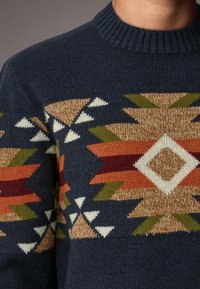 Marineblauwe wollen trui met een geometrisch patroon in beige, oranje, groen en bordeauxrood, voorzien van een geribde ronde hals en een gestructureerde brei.
