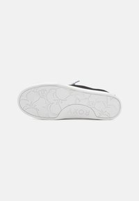 Schwarzer Schuh mit einer weißen Sohle, die Blumenmuster aufweist. Die Sohle hat den Markennamen 'ROXY' eingeprägt. Minimalistisches Design mit einer glatten Textur.