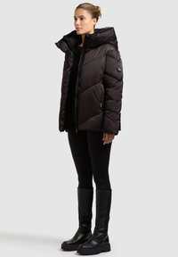 Black puffer jacket with a high collar and quilted design, featuring a zip closure and side pockets. Paired with black leggings and knee-high boots.