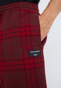 Pantalons en plaid rouge et marron en tissu doux, dotés d'une taille élastique et d'une étiquette noire avec le texte "BJÖRN BORG".