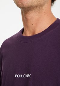 Lilla bomulds T-shirt med rund halsudskæring og broderet "VOLCOM" logo i hvid på brystet. Glat tekstur.