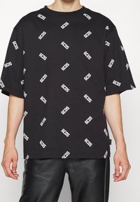 Camiseta oversized de algodón negra con un diseño de logotipo "GCSD" en blanco repetido. Cuello redondo y mangas cortas con un corte relajado.