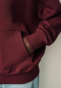 Bordeauxroter Pullover mit Fronttasche, gerippten Bündchen und Saum. Weicher Stoff mit lässigem Schnitt und entspannter Passform.
