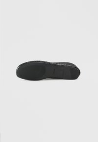 Espadrilla nera con tomaia intrecciata, suola piatta in gomma e dettagli testurizzati. Presenta un logo discreto vicino al tallone.