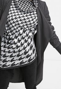 Czarnobiały top w wzór pepitki, o luźnym kroju, z czarną warstwą zewnętrzną. Tkanina wydaje się miękka; faktura jest gładka, z dekoltem typu komin.