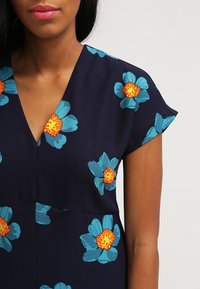 Vestido floral con un fondo azul marino adornado con grandes flores turquesa y centros naranjas; de mangas cortas y diseño de escote en V.
