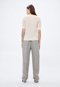 Jasnobeżowa bluzka z krótkim rękawem wykonana z miękkiej tkaniny, zestawiona z szarymi, szerokimi spodniami o fakturowanej powierzchni, charakteryzującymi się luźnym krojem i podwiniętymi rękawami.