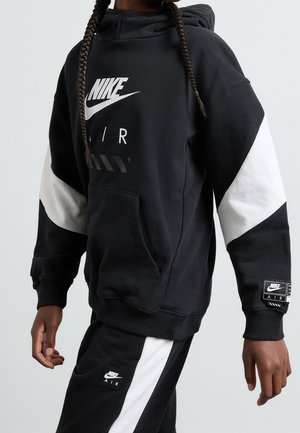 Sort Nike-hoodie med hvide detaljer, som har stort logo, kængurulomme og tekstureret stof. Kombination med sorte bukser med logodetalje.