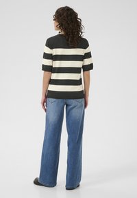 Haut à manches courtes rayé en gris foncé et crème, associé à un jean bleu ample. Tissu léger, coupe décontractée et design de pantalons à jambe droite.