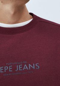 Felpa bordeaux con girocollo a coste, con logo stampato in testo grigio sul davanti, realizzata in morbido tessuto misto cotone.