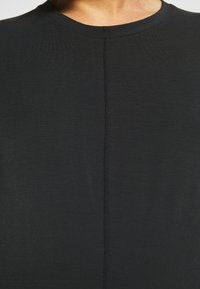 Zbliżenie osoby noszącej czarną koszulę z centralnym pionowym szwem i okrągłym dekoltem.