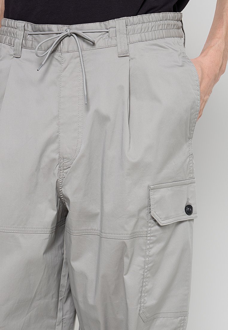 Pantalones cargo gris claro fabricados con una tela lisa y ligera, con cinturilla elástica, cordón y un bolsillo lateral con botón.