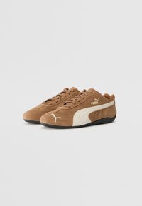 Braune Wildleder-Sneaker mit weißen Akzenten, ausgestattet mit einer schwarzen Gummisohle, Schnürverschluss und Puma-Logo an der Seite und Zunge.